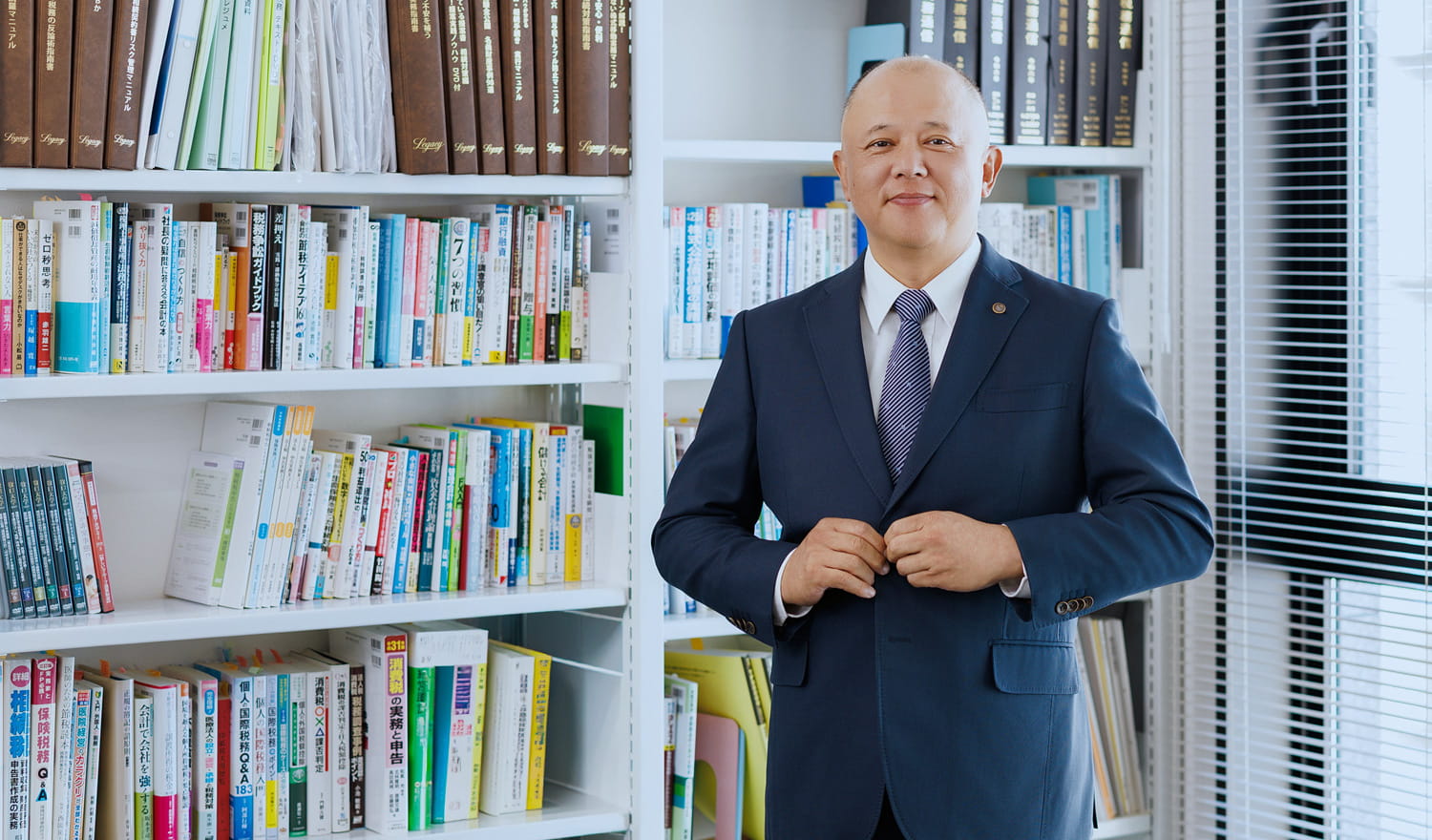 スーツの上着のボタンに手をかけ笑顔の菊地税理士事務所の所長・菊地正和